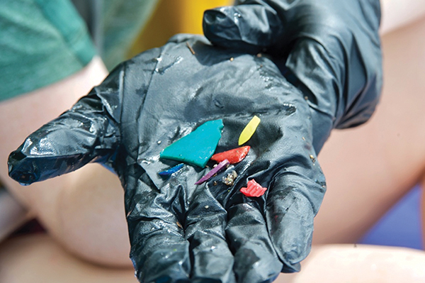 A gloved hand holds small colorful pieces of microplastic..