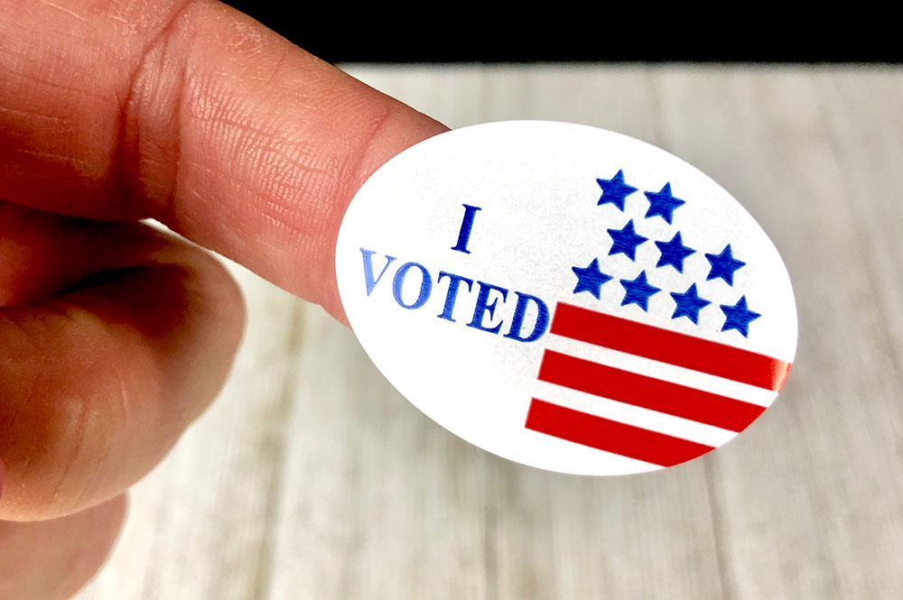 A person holds an "I Voted" sticker on their fingertip.