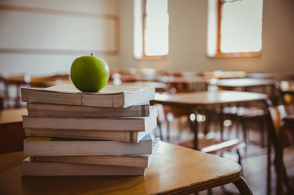 An apple sits on top of a stack of books in an empty classroom.