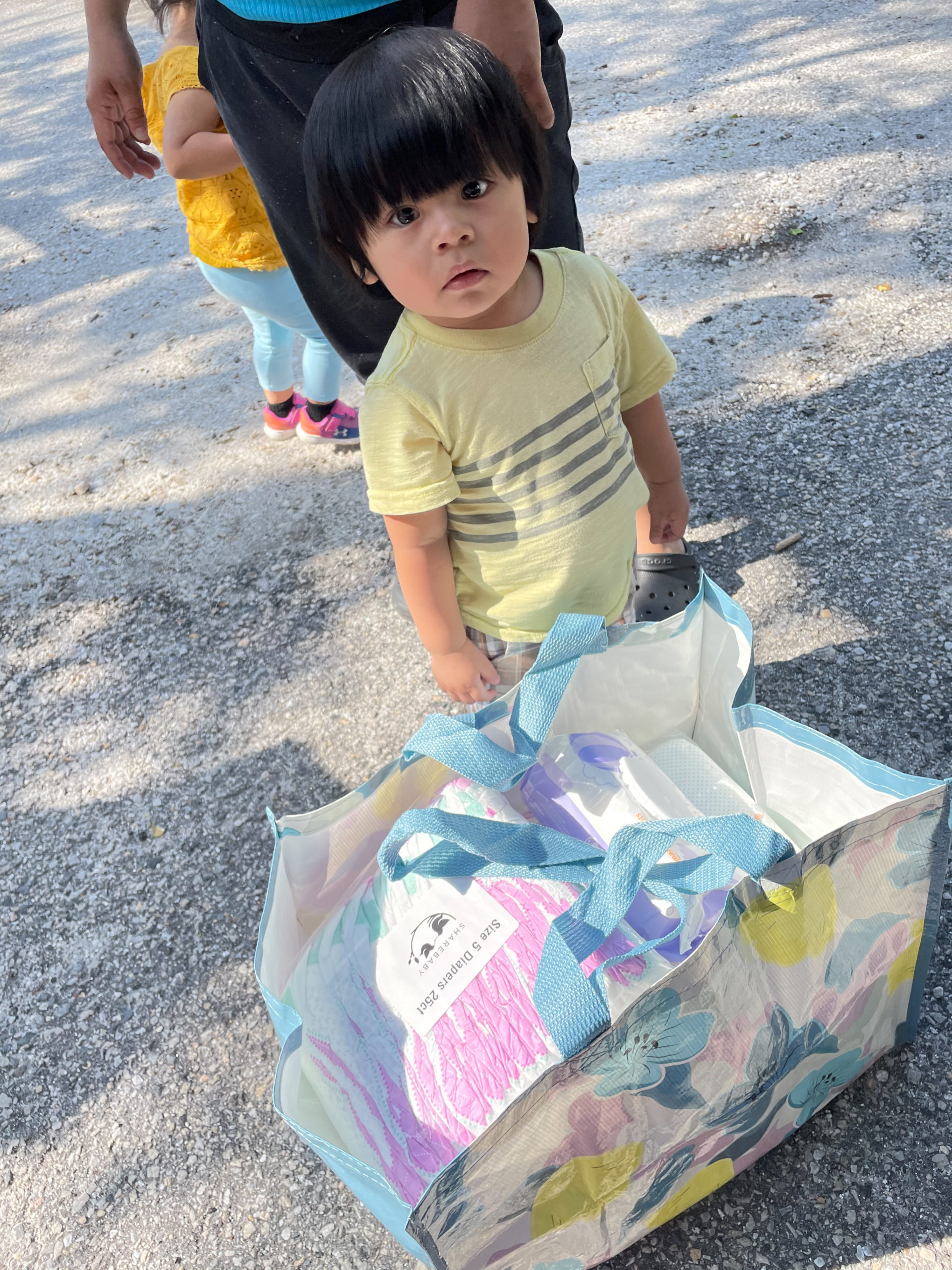 A young child stands above a tote filled with diapers.
