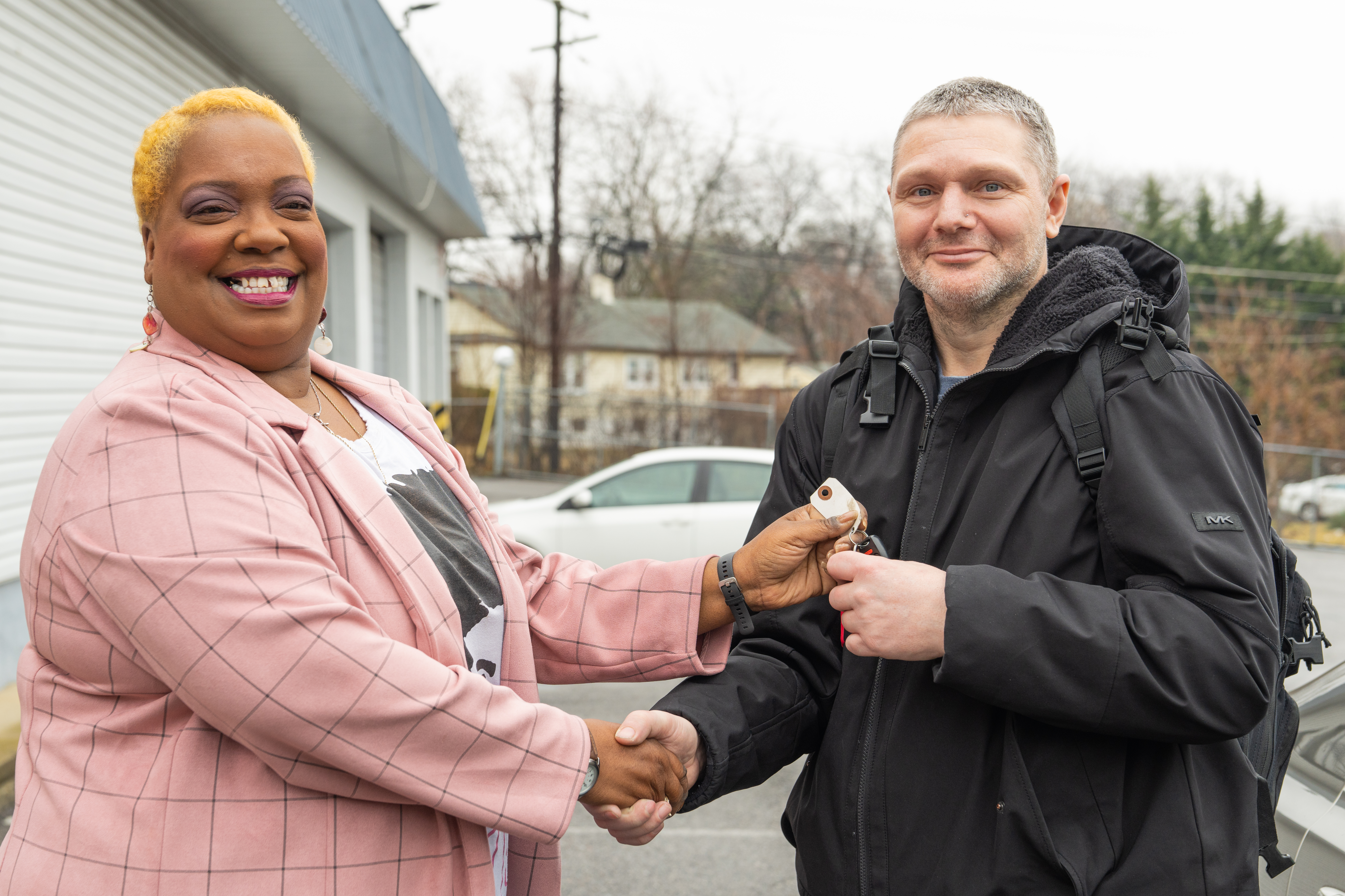 A woman hands a man car keys and shakes his hand