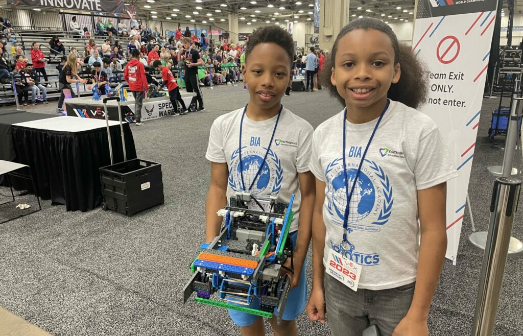 Two students hold their robots at a robotics competition.